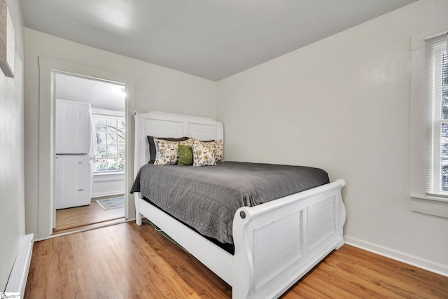 bedroom with light wood-style floors, baseboards, and baseboard heating