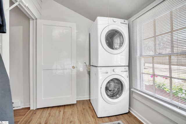 clothes washing area with laundry area, baseboards, stacked washer / drying machine, and light wood finished floors