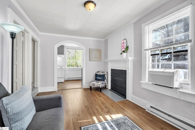 living room with a baseboard radiator, arched walkways, wood finished floors, and crown molding