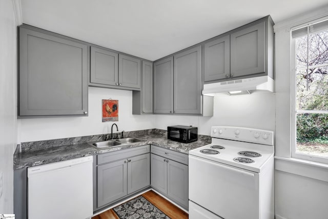 kitchen featuring gray cabinets, under cabinet range hood, a sink, dark countertops, and white appliances