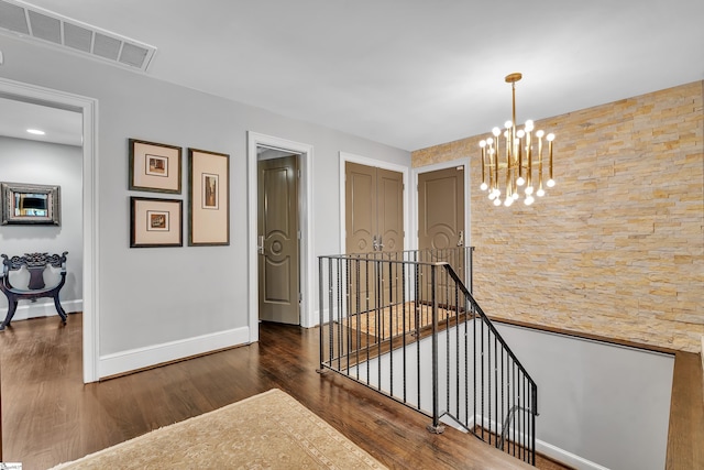 hall with visible vents, an upstairs landing, wood finished floors, baseboards, and a chandelier