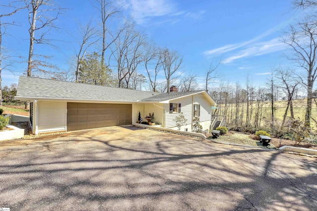 view of front of home with aphalt driveway, an attached garage, roof with shingles, and a chimney