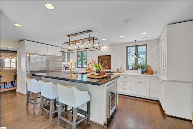 kitchen featuring visible vents, a sink, dark wood finished floors, white cabinets, and a kitchen island with sink