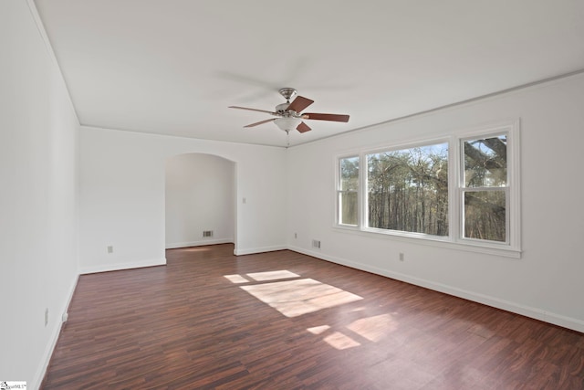 empty room with arched walkways, dark wood finished floors, baseboards, and ceiling fan