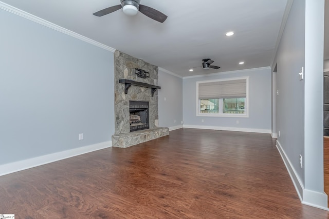 unfurnished living room with a ceiling fan, dark wood finished floors, a stone fireplace, crown molding, and baseboards