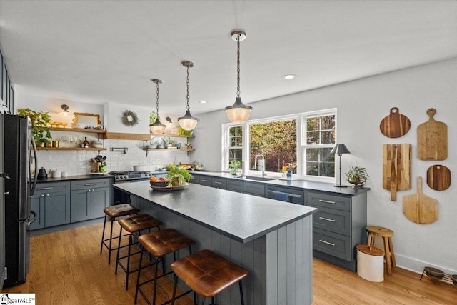 kitchen with gas stove, open shelves, freestanding refrigerator, a sink, and dark countertops