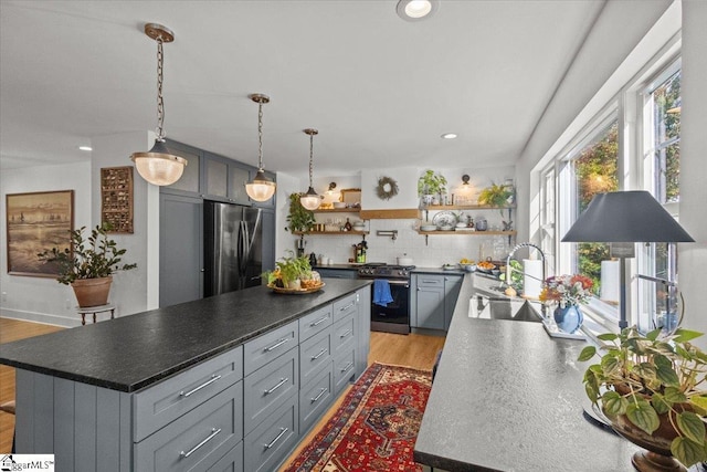 kitchen featuring open shelves, a sink, stainless steel appliances, light wood-style floors, and a center island