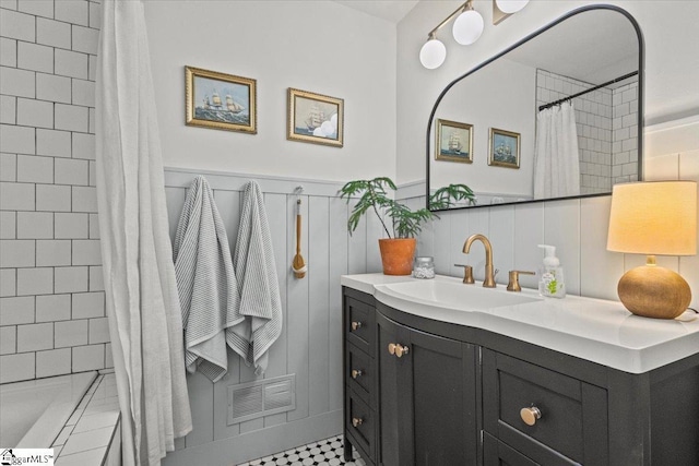 bathroom featuring visible vents, wainscoting, tiled shower, and vanity