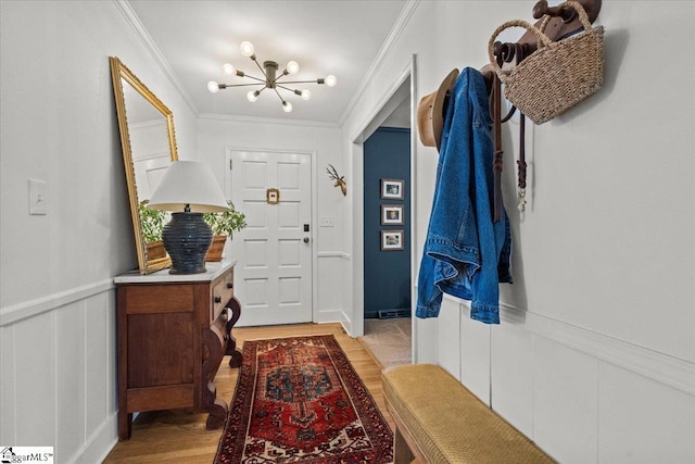 entryway featuring light wood-type flooring, ornamental molding, wainscoting, an inviting chandelier, and a decorative wall