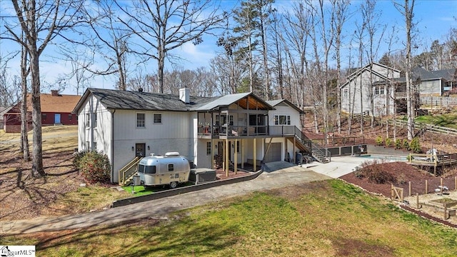 back of house with stairway, driveway, a wooden deck, a chimney, and a garage