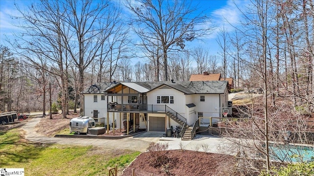 rear view of property with stairway, a garage, concrete driveway, and a chimney