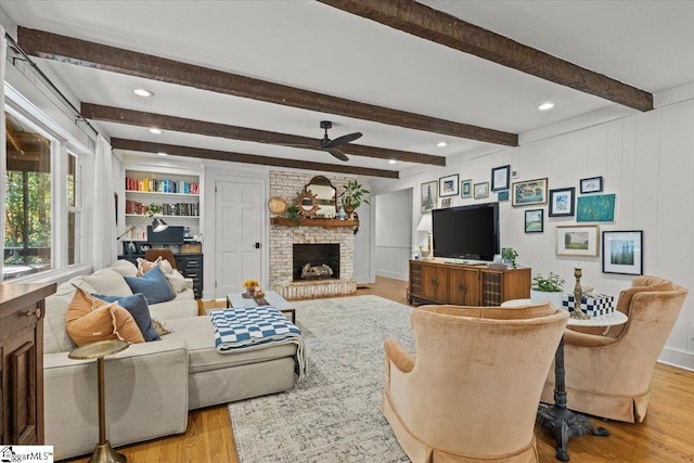 living area featuring beamed ceiling, a brick fireplace, a ceiling fan, and wood finished floors