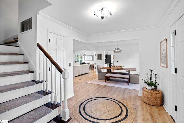 foyer entrance with crown molding, light wood-style flooring, stairway, and visible vents