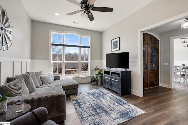 living area with a wainscoted wall, a ceiling fan, visible vents, and dark wood-style flooring