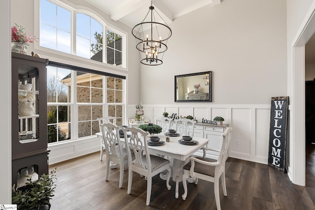 dining space featuring beam ceiling, dark wood-type flooring, an inviting chandelier, and a decorative wall