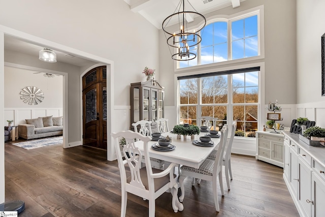 dining area with arched walkways, a chandelier, dark wood finished floors, and wainscoting