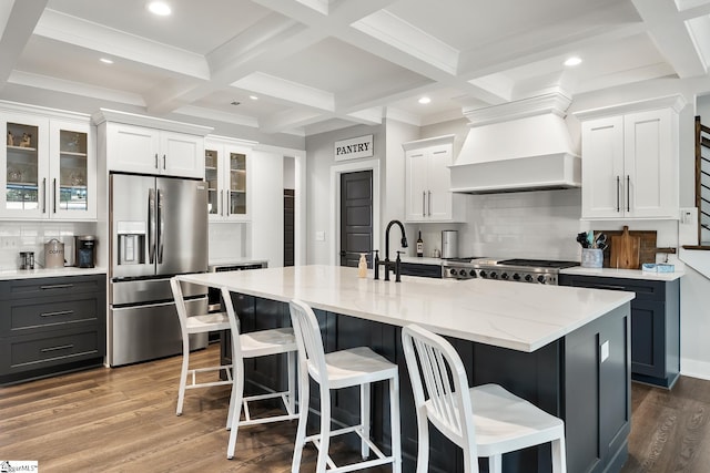 kitchen featuring glass insert cabinets, beamed ceiling, custom range hood, stainless steel refrigerator with ice dispenser, and wood finished floors