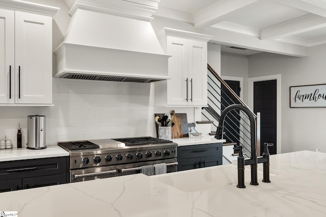 kitchen featuring custom exhaust hood, range with two ovens, white cabinets, and beam ceiling