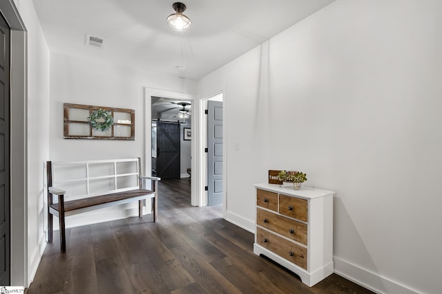 hallway with a barn door, baseboards, visible vents, and dark wood-style flooring