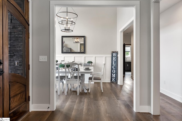 hallway featuring dark wood finished floors, a decorative wall, baseboards, and an inviting chandelier