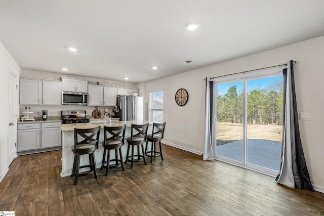 kitchen with a breakfast bar area, dark wood-type flooring, appliances with stainless steel finishes, and a kitchen island with sink