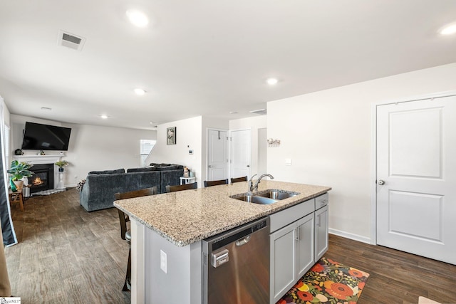 kitchen featuring a glass covered fireplace, light stone countertops, dark wood-style flooring, a sink, and stainless steel dishwasher