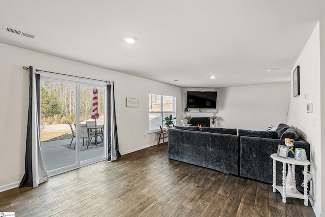 living area featuring baseboards, visible vents, recessed lighting, a lit fireplace, and dark wood-type flooring