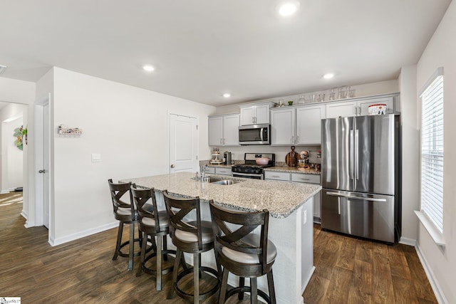 kitchen featuring a center island with sink, light stone counters, a kitchen breakfast bar, stainless steel appliances, and dark wood-style flooring