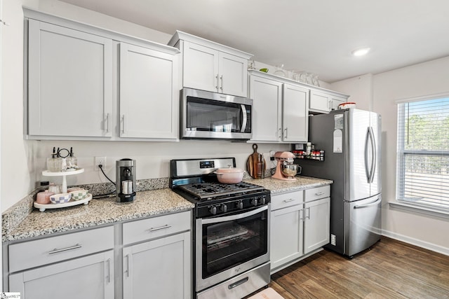 kitchen with baseboards, dark wood finished floors, light stone counters, recessed lighting, and appliances with stainless steel finishes