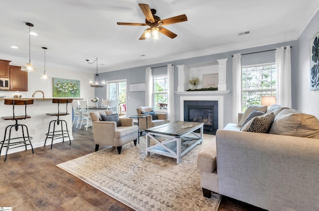 living room featuring a ceiling fan, visible vents, dark wood finished floors, a glass covered fireplace, and crown molding