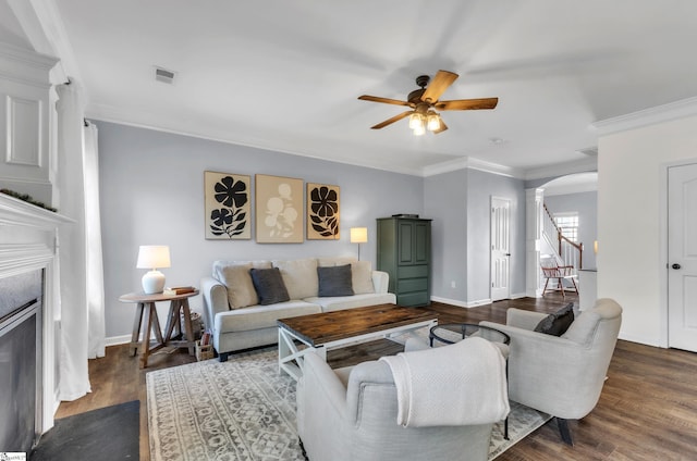 living room featuring crown molding, stairway, a fireplace, wood finished floors, and arched walkways