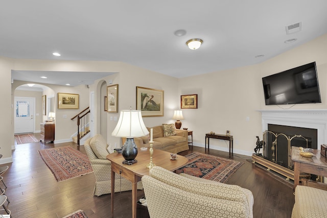 living room featuring visible vents, baseboards, a fireplace, arched walkways, and dark wood-style flooring