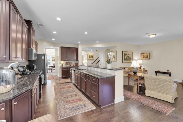 kitchen featuring visible vents, dark wood-type flooring, dark stone countertops, stainless steel appliances, and a sink