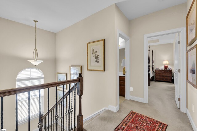 hall with baseboards, an upstairs landing, and light colored carpet