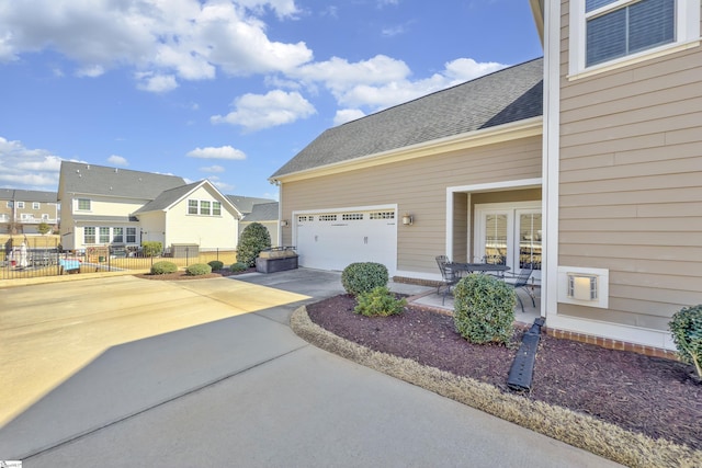 exterior space with fence, roof with shingles, an attached garage, concrete driveway, and a residential view