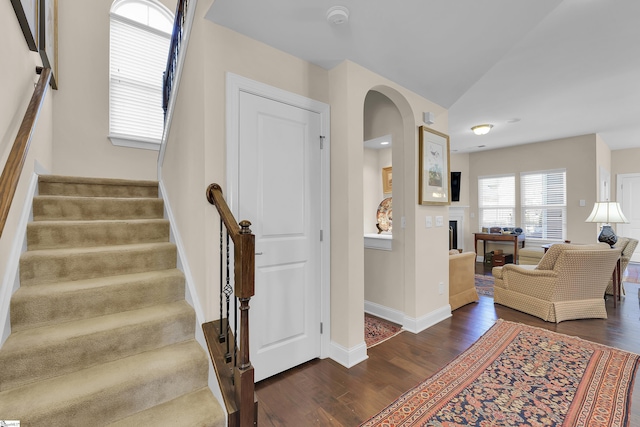 stairway featuring baseboards, wood finished floors, a fireplace, and vaulted ceiling