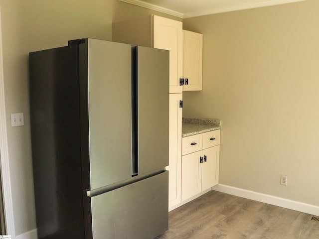 kitchen with baseboards, light stone counters, freestanding refrigerator, light wood-style floors, and white cabinets