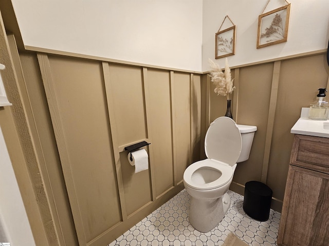 bathroom featuring a decorative wall, toilet, and vanity