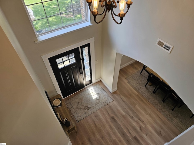 foyer with visible vents, wood finished floors, a towering ceiling, baseboards, and a chandelier