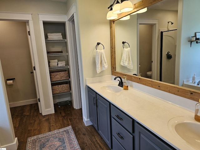 full bathroom featuring wood finished floors, double vanity, a stall shower, a sink, and toilet