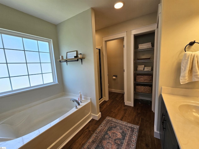 bathroom with a garden tub, wood finished floors, a shower stall, baseboards, and vanity