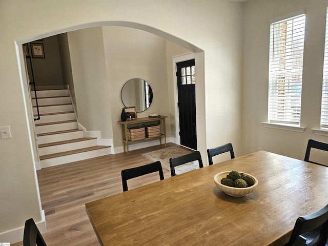 dining room featuring arched walkways, a healthy amount of sunlight, wood finished floors, and stairs