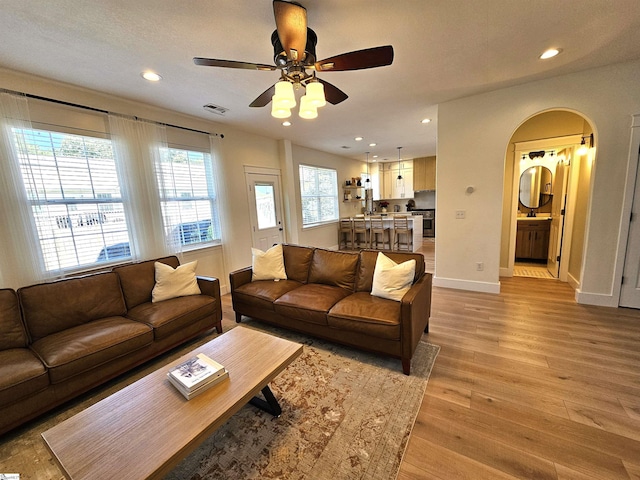 living area with visible vents, baseboards, recessed lighting, arched walkways, and light wood-style floors