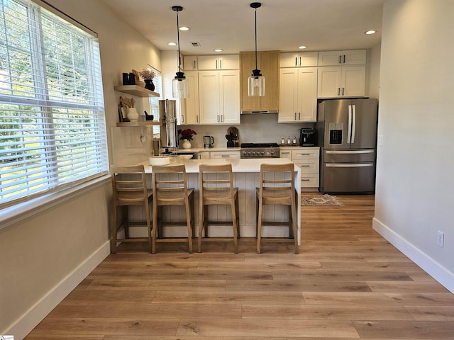 kitchen with baseboards, decorative light fixtures, appliances with stainless steel finishes, a peninsula, and light wood-style floors