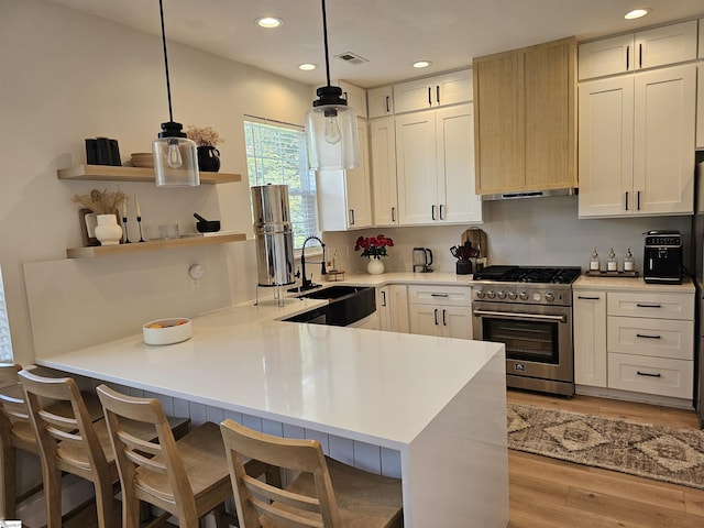 kitchen with light countertops, a peninsula, light wood-style floors, stainless steel stove, and white cabinets