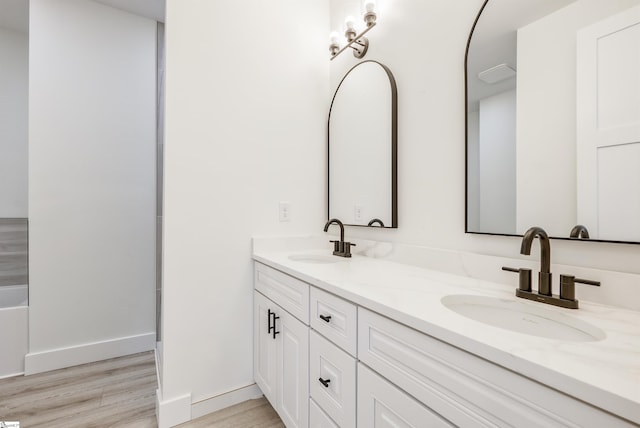 bathroom featuring double vanity, wood finished floors, baseboards, and a sink