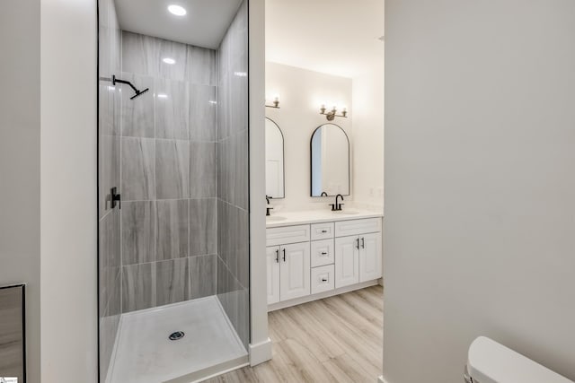 full bath featuring wood finished floors, tiled shower, double vanity, a sink, and toilet