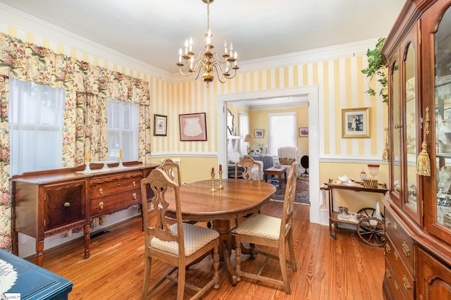 dining space featuring light wood-type flooring, an inviting chandelier, ornamental molding, and wallpapered walls