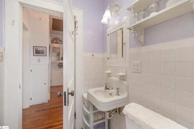 half bath with a sink, tile walls, a wainscoted wall, and wood finished floors