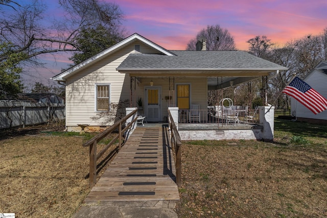 bungalow-style home featuring a shingled roof, a yard, and fence